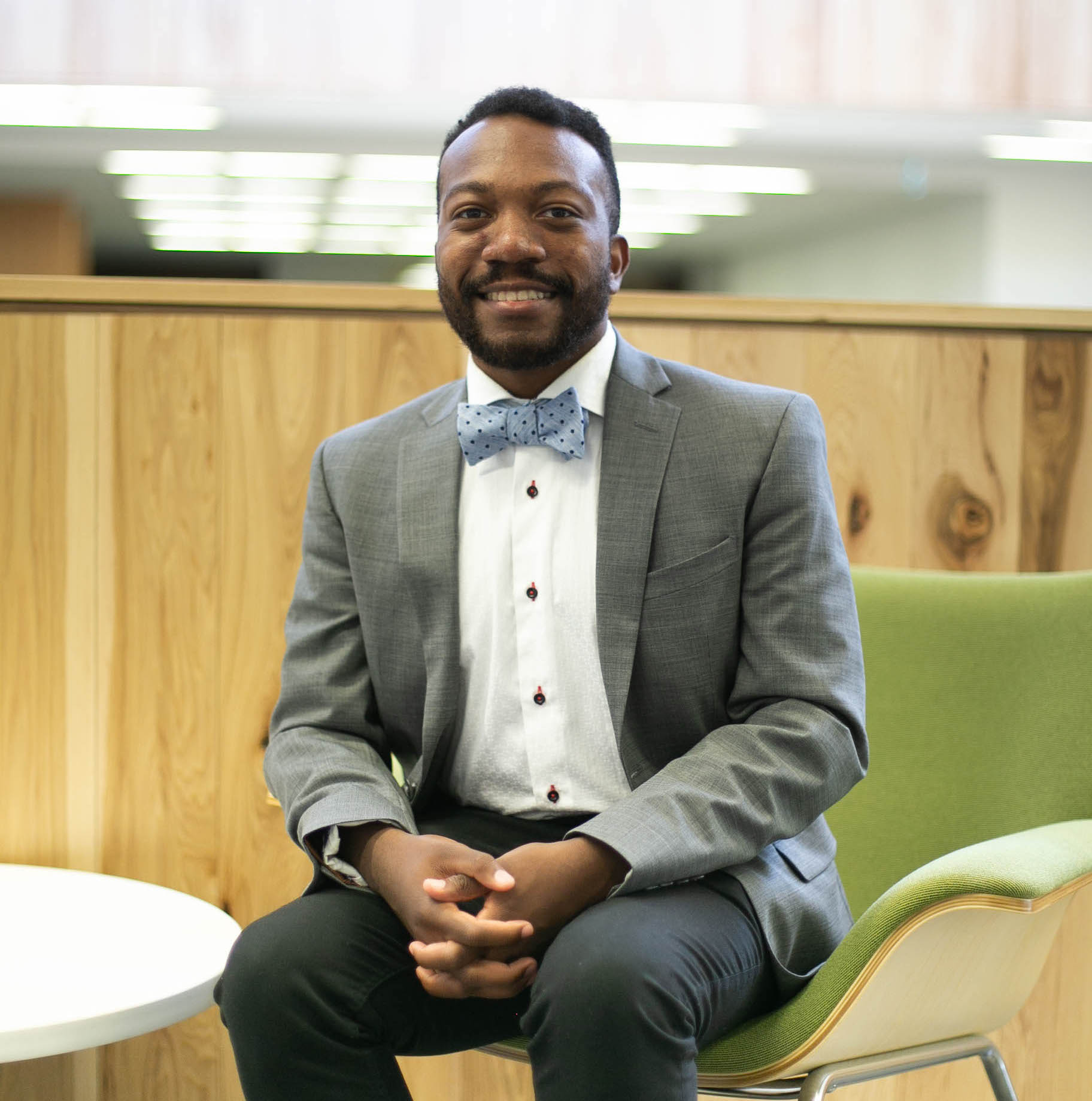 A male student who is wearing a suit is sitting on a chair